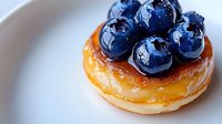 Fresh blueberries on glazed mini donut dessert with golden caramel topping on white plate, macro food photography with selective focus and blur.