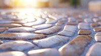 Sunlit cobblestone path with smooth rounded stones creating natural pattern texture, morning light casting warm glow and soft shadows across weathered surface.