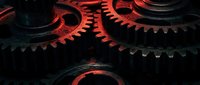 Industrial metal gears with red lighting creating dramatic mechanical engineering concept for manufacturing and technology backgrounds.