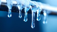 Frozen icicles with water drops in blue winter light, macro close-up showing crystalline structure and melting droplets forming on transparent ice formations.