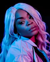 Young African American woman with long blonde wavy hair in neon lighting, wearing white jacket. Dramatic portrait with blue and pink color gels creating vibrant duotone effect.