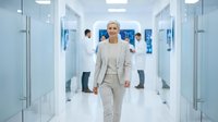Mature Caucasian male professional in beige business suit walking confidently through modern hospital corridor with medical staff in background, suitable for healthcare, corporate wellness, and medical facility concepts.