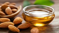 Sweet almond oil in glass bowl with raw almonds on wooden surface, natural skincare and aromatherapy ingredients for wellness and beauty treatments.