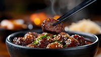Glazed Asian meatballs with sesame seeds and green onions in black ceramic bowl, chopsticks holding piece. Dark moody background with bokeh lights creates appetizing atmosphere.