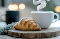 Fresh baked croissant on wooden board with steaming hot coffee cup and pine branch, morning breakfast scene with soft bokeh background.