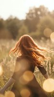 Young woman with flowing red hair dancing in golden sunset light with bokeh effects in natural meadow setting for lifestyle and wellness concepts.