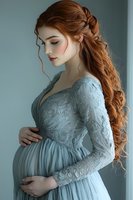 Pregnant woman with long red hair in elegant blue lace dress touching belly, maternity portrait for motherhood and pregnancy concepts.