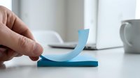 Hand holding blue upward arrow symbol on white desk with office supplies, representing growth, success, and positive business progress in corporate environment.