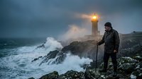 Photographer capturing dramatic lighthouse scene during storm with crashing waves on rocky coastline at dusk for adventure travel content.