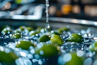 Fresh green grapes being washed under running water with sparkling droplets and bokeh effect, macro food photography showing produce cleaning process.