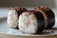 Fresh sushi rolls with white rice, dark nori seaweed wrap, topped with sesame seeds and red spice flakes, served on white plate, macro food photography.