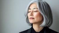 Serene mature Asian woman with elegant gray bob hairstyle and closed eyes against neutral background, portraying confidence and tranquility.