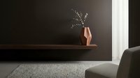 Minimalist interior with copper geometric vase holding dried foliage on floating wooden shelf against dark wall, modern home decor styling.