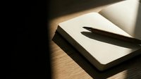 Open notebook with two black markers on wooden desk surface, illuminated by natural light, suitable for creative writing, design, education, and office projects.