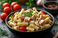 Creamy pasta salad with tuna chunks, cherry tomatoes, fresh dill, and rigatoni in black ceramic bowl. Mediterranean style dish on dark background with ingredients.