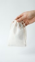 Hand holding a small natural cotton drawstring bag on a light background, eco-friendly packaging for gifts, jewelry, or handmade products.