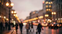 Blurred city street at dusk with warm golden lights and pedestrians walking, creating atmospheric bokeh effect for urban lifestyle concepts.