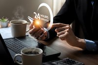 Businessman hands holding glowing 24 hours service icon above laptop computer on wooden desk with coffee cups in modern office workspace for customer support.