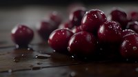 Fresh ripe cranberries scattered on dark wooden surface with water drops and moody lighting, macro food photography for harvest season and cooking.