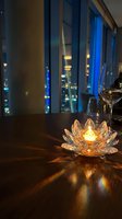 Crystal lotus candle holder glowing on wooden table with wine glasses and city lights through windows creating romantic dining atmosphere.