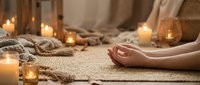Woman practicing meditation in cozy candlelit room with warm blankets and peaceful atmosphere for mindfulness and relaxation wellness lifestyle.