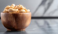 Raw cashew nuts in wooden bowl on dark background with copy space, selective focus on nutritious protein-rich snack for healthy eating.