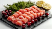 Fresh raw salmon sashimi slices arranged on black stone plate with cranberries, dill herbs and lemon. Luxurious seafood appetizer for restaurant menu.