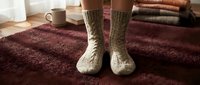 Cozy knitted wool socks on burgundy carpet with coffee mug and books creating warm comfortable home atmosphere for relaxation and leisure time.