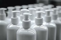 White plastic pump bottles arranged in rows, selective focus on front dispenser against blurred background creates minimalist composition for cosmetic packaging.