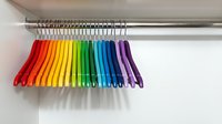 Colorful rainbow clothes hangers arranged in order on a silver rod in a white closet, showcasing vibrant organization and home storage.