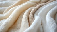 Soft cream-colored fleece fabric with gentle folds and textural details creates cozy, warm feeling. Close-up macro photography shows plush material surface.