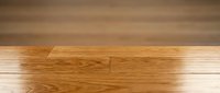 Polished hardwood floor planks with natural wood grain pattern and warm honey oak finish meeting white baseboard trim in modern interior home design.