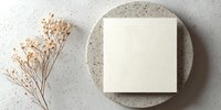 Blank cream square card on textured ceramic plate with dried gypsophila flower against neutral stone background. Minimalist stationery mockup.