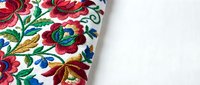 Traditional folk embroidery with colorful floral patterns on white fabric, featuring red roses and green leaves for textile and craft projects.