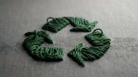 Green yarn threads arranged in recycling symbol shape on fabric background representing eco-friendly sustainable textile production and environmental awareness.