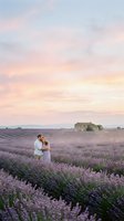 Couple embracing in blooming lavender field at sunset with rustic stone farmhouse in background, romantic countryside landscape for wedding and travel photography.