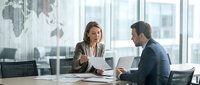 Professional businesswoman and businessman discussing strategy in modern conference room with world map and city view for corporate presentations.
