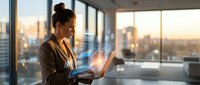 Professional businesswoman using laptop with digital interface icons in modern office overlooking city skyline at sunset for technology and business concepts.