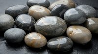 Smooth polished river stones in natural earth tones scattered on dark slate surface for spa wellness meditation zen garden landscaping home decor projects.