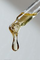 Golden viscous liquid dripping in slow motion creates elegant fluid shape with suspended droplet against light gray background, capturing surface tension dynamics.