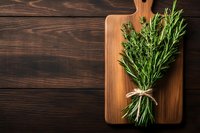 Fresh rosemary bunch tied with twine on wooden cutting board against dark rustic table background. Natural cooking ingredients for food blogs.