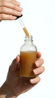 Hands applying golden serum with dropper to glass bottle on white background for skincare and beauty product packaging design.