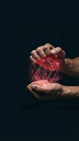 Male hands protecting glowing red geometric hologram cube with digital wireframe structure on dark background for technology and innovation concepts.
