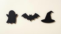 Black paper Halloween silhouettes featuring ghost, bat and witch hat on cream background for seasonal decorations and craft projects.