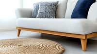 Modern living room with white scandinavian sofa, wooden legs, decorative pillows in navy blue and zigzag pattern, and round natural jute rug on light floor.