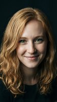 Portrait of smiling blonde woman with green eyes and wavy hair against dark background for professional headshots and business marketing materials.
