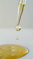 Macro shot of golden liquid drops falling from pipette onto surface, capturing moment of suspension with precise focus and soft background for scientific concept.