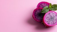 Vibrant pink dragon fruit slices with black seeds and fresh mint leaves arranged on pink background, showcasing exotic tropical fruit texture and natural patterns.