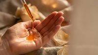 Natural skincare serum drops from glass dropper into cupped hands with warm golden sunlight creating luxurious spa atmosphere for beauty routine.