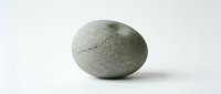 Cracked gray stone egg with textured surface on white background, symbolizing new beginnings, fragility, and natural birth concepts for creative projects.